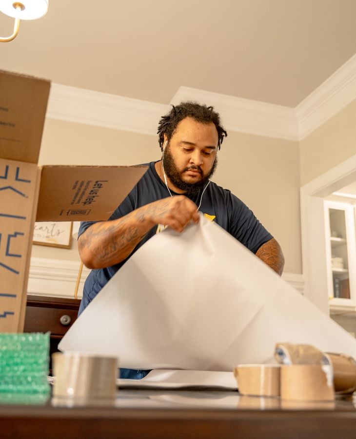 Electric City Movers LLC crew member carefully wrapping items with packing paper next to moving boxes during a professional packing service in a residential home in Anderson, SC