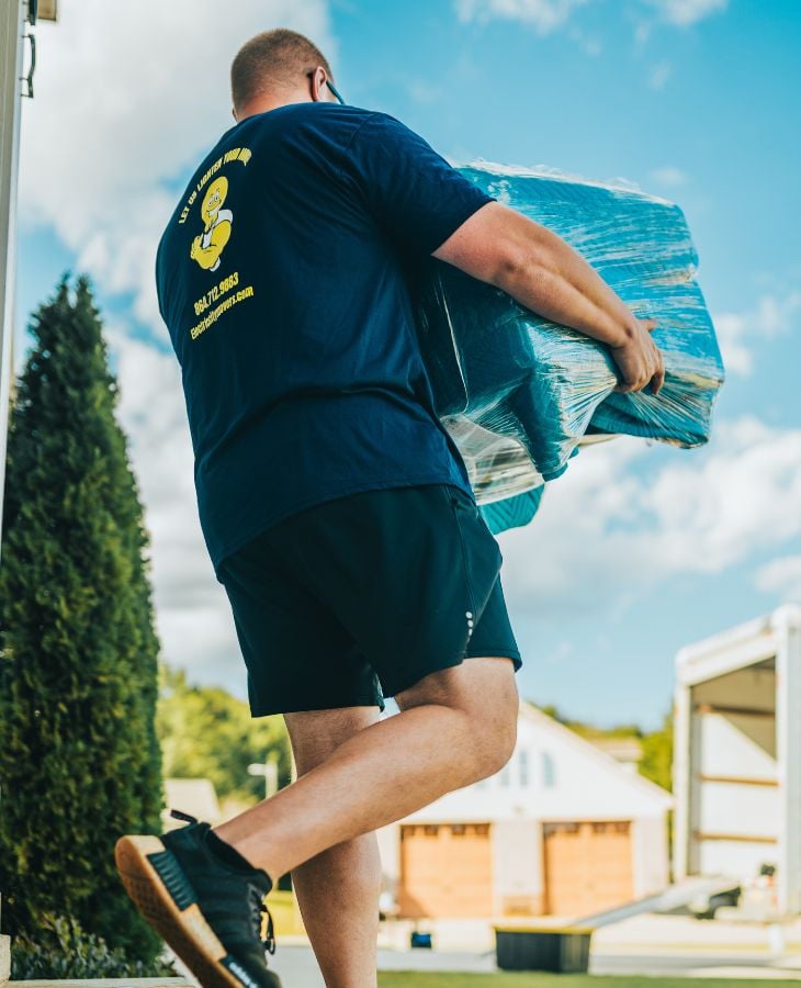 Electric City Movers LLC crew member carrying a plastic-wrapped item while walking toward a residential home during a local move in Anderson, SC