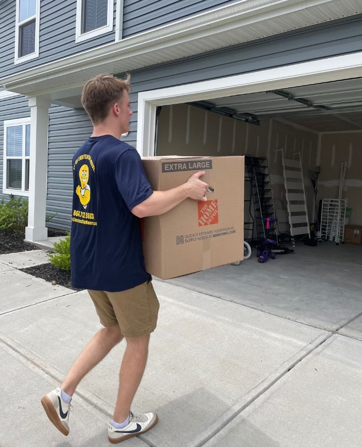 Electric City Movers LLC crew member carrying an extra large moving box toward the garage of a residential home during a local move in Anderson, SC
