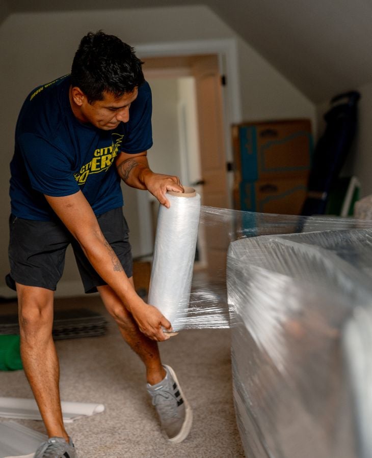 Electric City Movers LLC crew member wrapping a large piece of furniture with plastic stretch wrap inside a residential room during a local move in Anderson, SC