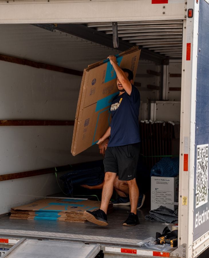 Electric City Movers LLC crew member lifting and loading a large cardboard box into the back of a moving truck during a residential or commercial move in Anderson, SC